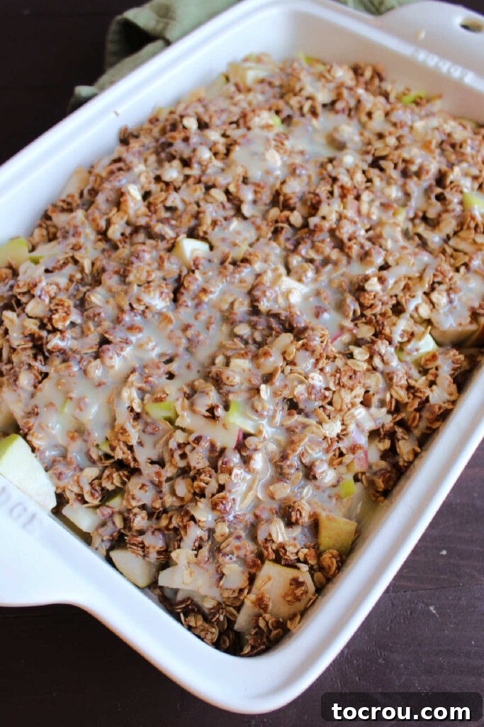 Pan of apple crisp with sweetened condensed milk drizzled over the top, ready to go in the oven.