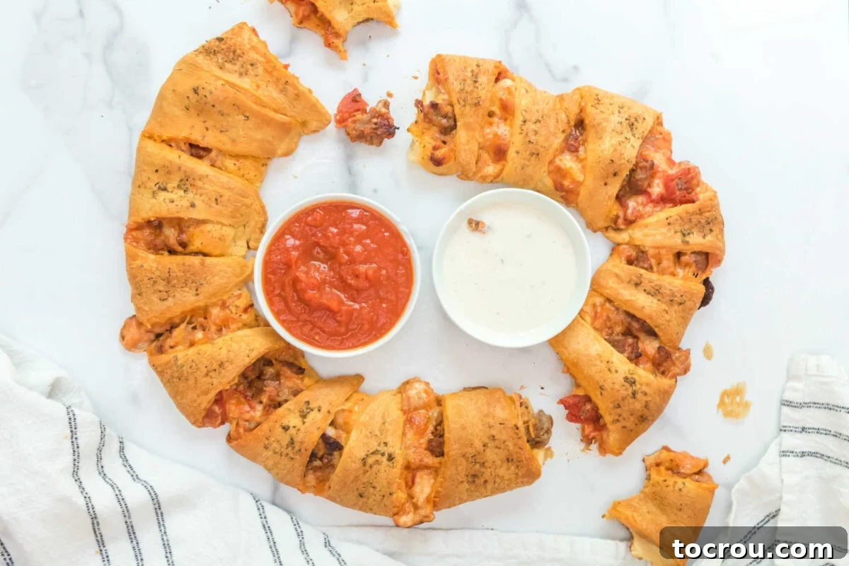 Ring made from crescent rolls and filled with pizza toppings served with a bowl of marinara sauce and a bowl of ranch dressing. 