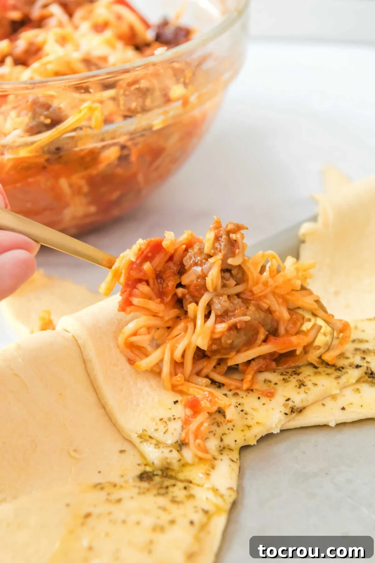 Spooning cheese, sausage, pepperoni and sauce mixture onto crescent dough.