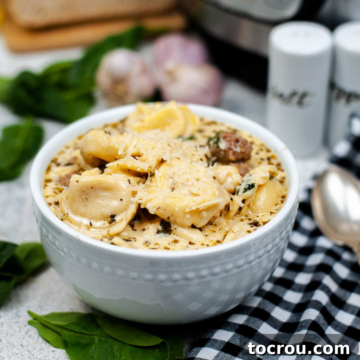 A steaming bowl of creamy tortellini sausage and spinach soup, garnished and ready to be enjoyed.