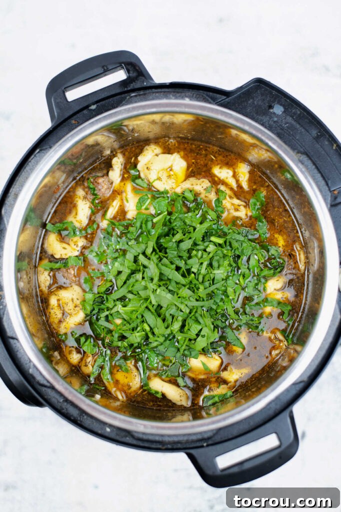 Chicken broth, cheese tortellini, and chopped spinach added to the Instant Pot, ready for pressure cooking.