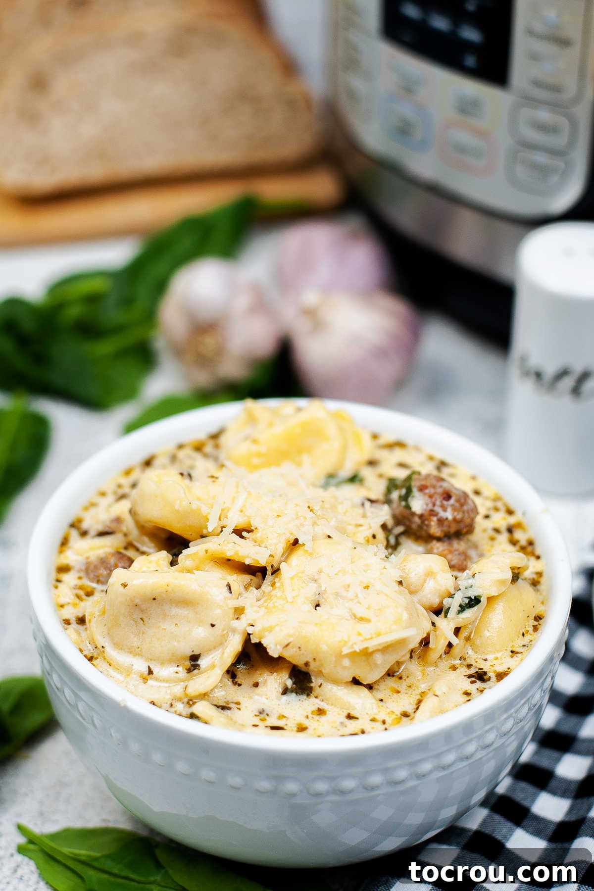 A bowl of creamy tortellini sausage and spinach soup, rich with cheese tortellini, Italian sausage chunks, and fresh spinach, placed in front of an Instant Pot.