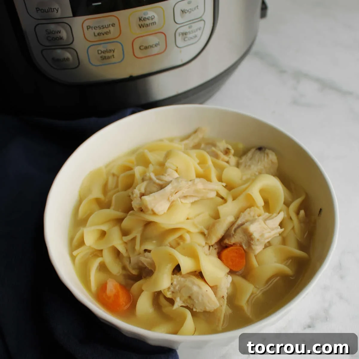 Flexible Chicken Noodle Soup: Instant Pot and Slow Cooker Ready 2 A comforting bowl of homemade chicken noodle soup, garnished with fresh parsley, in front of a modern instant pot, highlighting its homemade freshness and the convenience of modern cooking appliances.