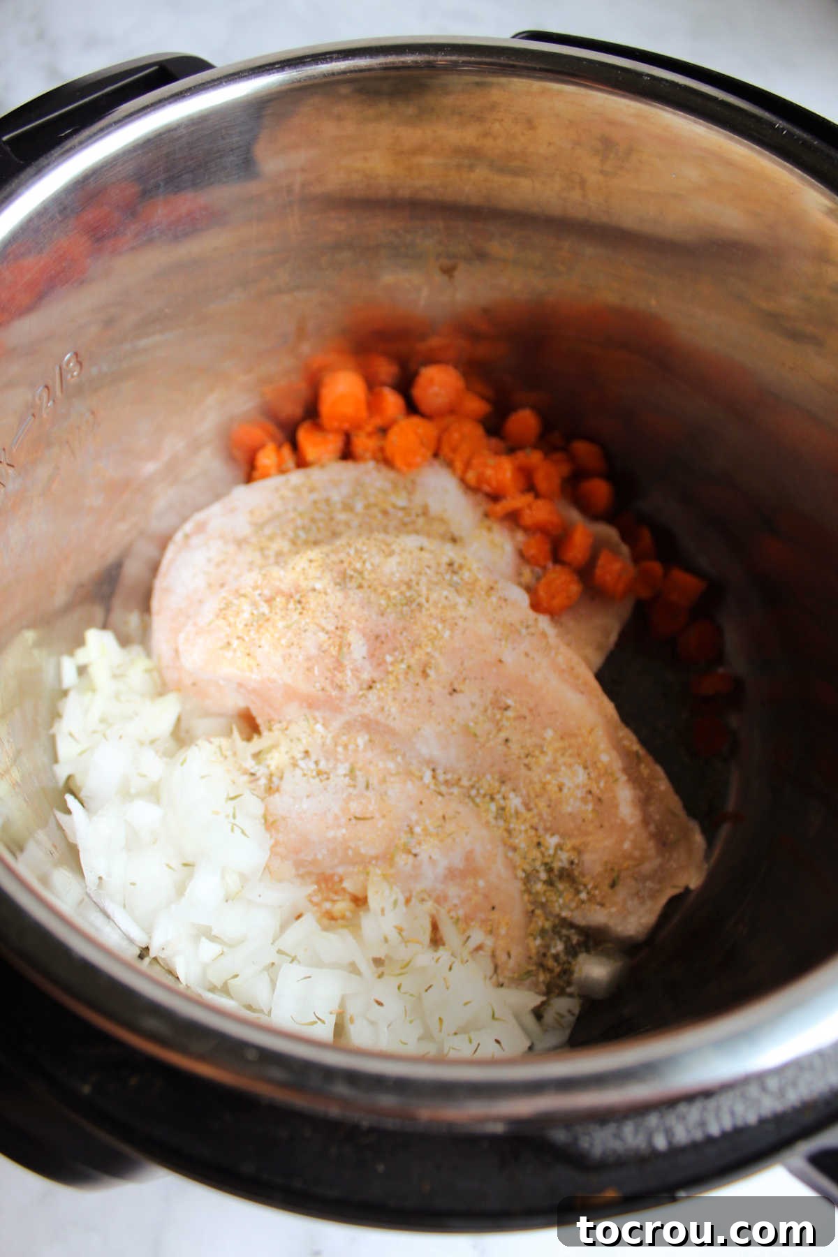 Flexible Chicken Noodle Soup: Instant Pot and Slow Cooker Ready 3 Frozen chicken breasts nestled with diced onion and vibrant carrots inside an Instant Pot, ready for pressure cooking, demonstrating the ease of starting with frozen ingredients.