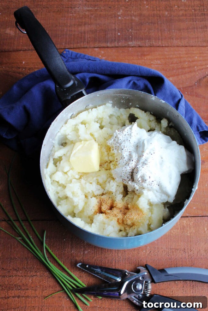 Sour Cream and Chive Smashed Potatoes 5 Pan of mashed potatoes with butter, sour cream and fresh chives on top ready to be mixed in.