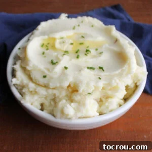 Serving bowl filled with creamy sour cream and chive mashed potatoes topped with extra melted butter and bits of fresh green chive.
