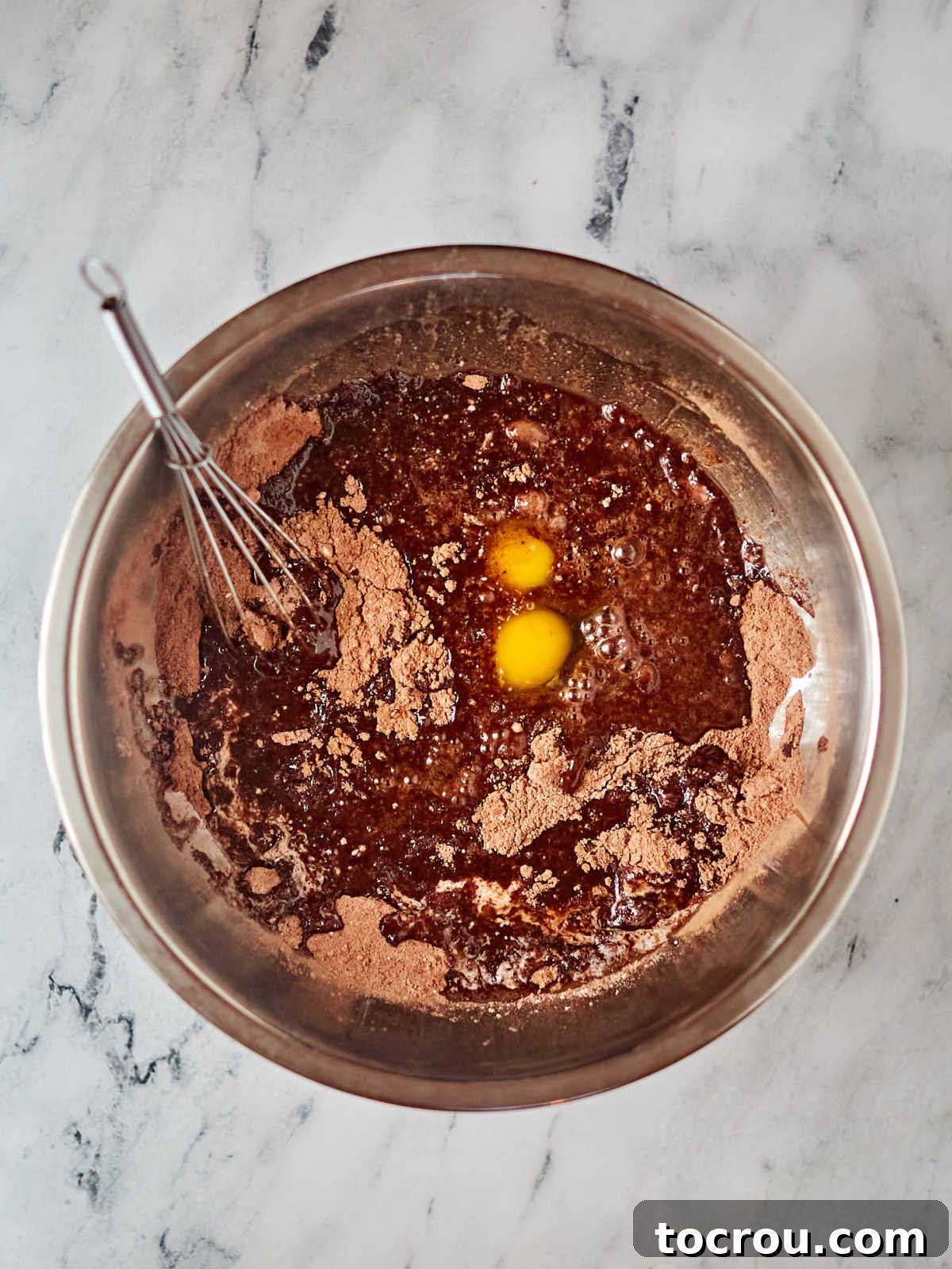 Adding Wet Ingredients to Brownie Mix A hand adding wet ingredients like eggs and vanilla to the dry brownie mix in a bowl, demonstrating the simple baking process.