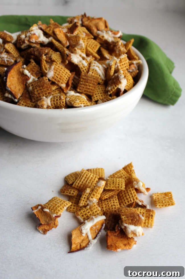 Bowl of apple cinnamon chex mix with some on the counter in front of it showing brown sugar coating and white chocolate drizzle.