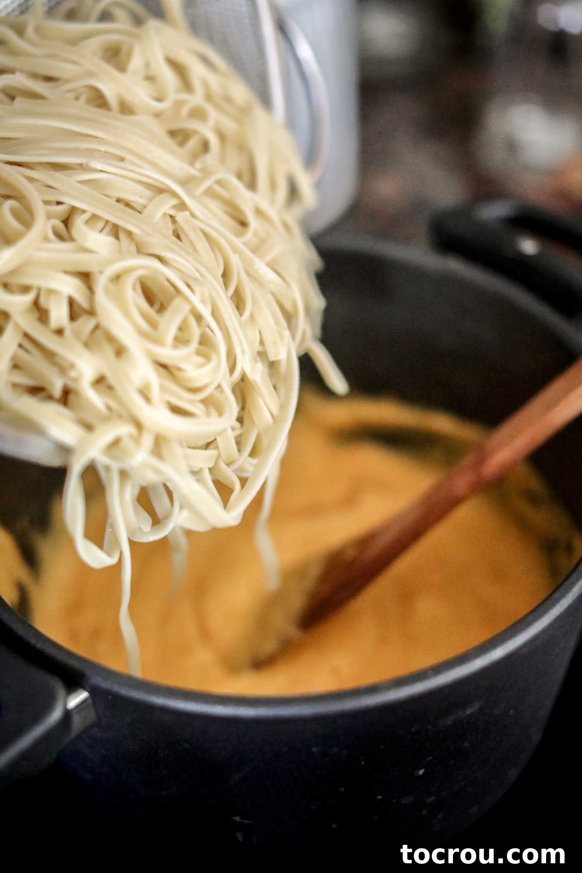 Drained pasta being poured directly into the prepared butternut squash alfredo sauce in a large pan, ready to be tossed and coated.