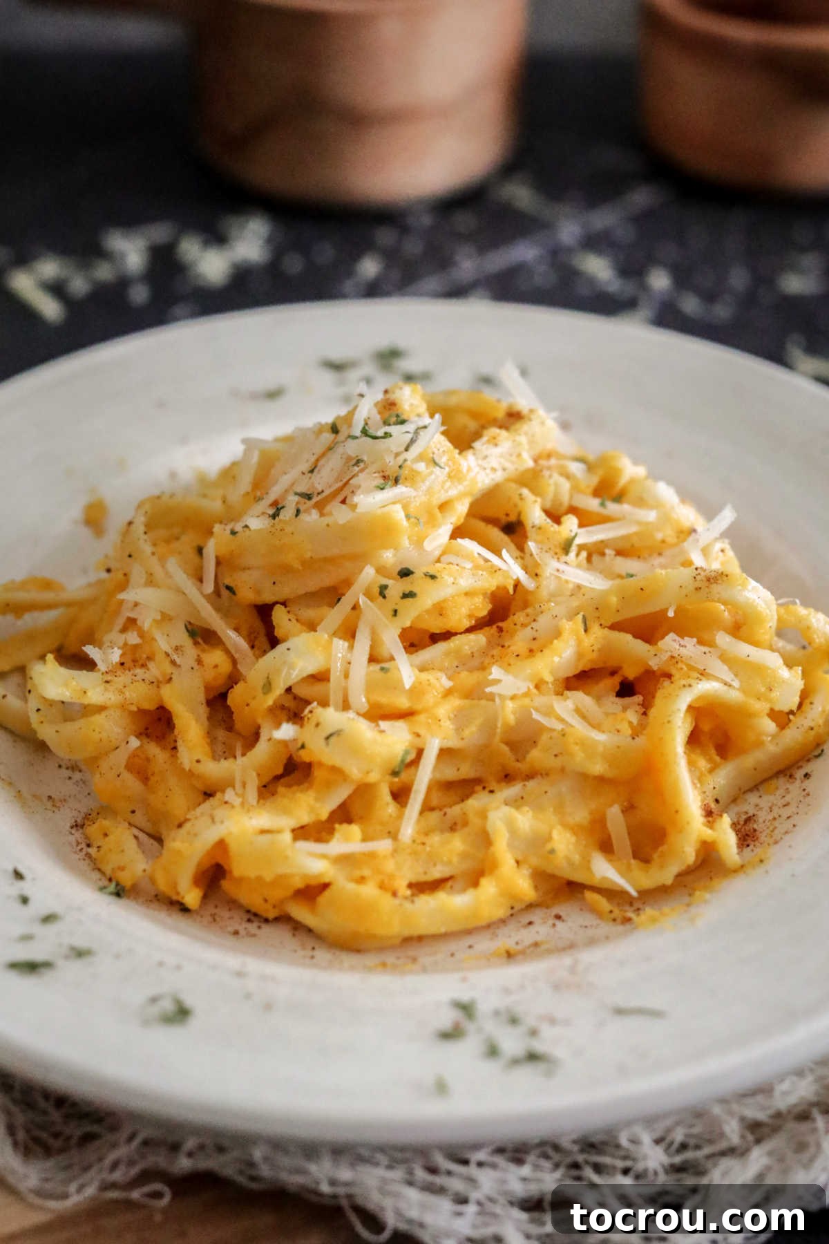 A close-up of a plate of fettuccine pasta generously coated in butternut squash alfredo sauce, finished with a fresh sprinkling of parsley.