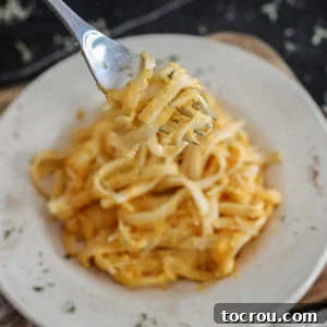 Fork filled with butternut squash alfredo sauce coated pasta ready to eat.