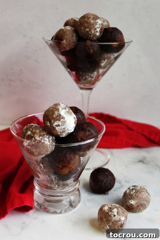 Kentucky Bourbon Pecan Truffles 4 Martini glasses filled with pecan bourbon balls, some coated in powdered sugar and others in cocoa powder, artistically arranged and ready to be enjoyed.