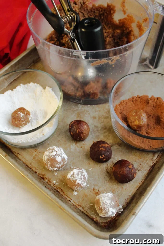 Kentucky Bourbon Pecan Truffles 7 A person rolling small, freshly formed bourbon balls in separate bowls, one containing powdered sugar and the other rich cocoa powder, for various coatings.