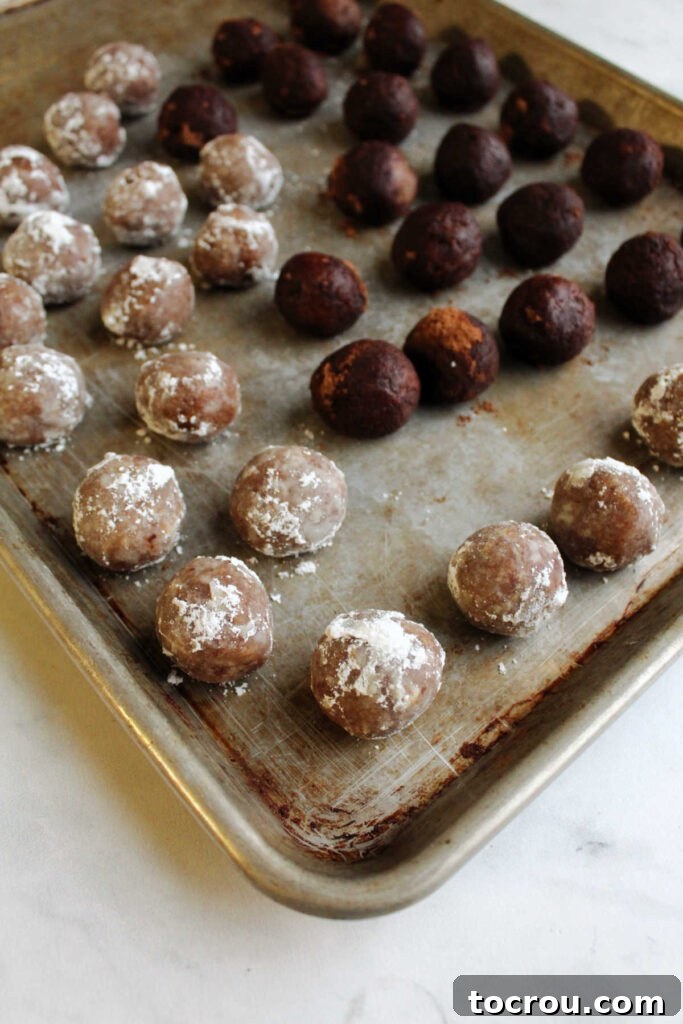 Kentucky Bourbon Pecan Truffles 8 A tray filled with freshly made bourbon balls, neatly arranged. Half are coated in powdered sugar, giving them a snowy look, and the other half are dusted with dark cocoa powder.