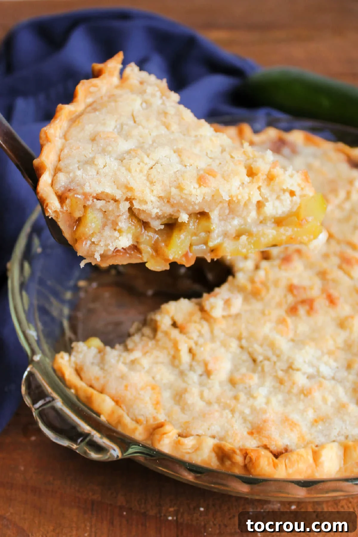 A perfect slice of mock apple pie, made with zucchini, is being carefully lifted from the pie plate, revealing its tantalizing cinnamon filling.