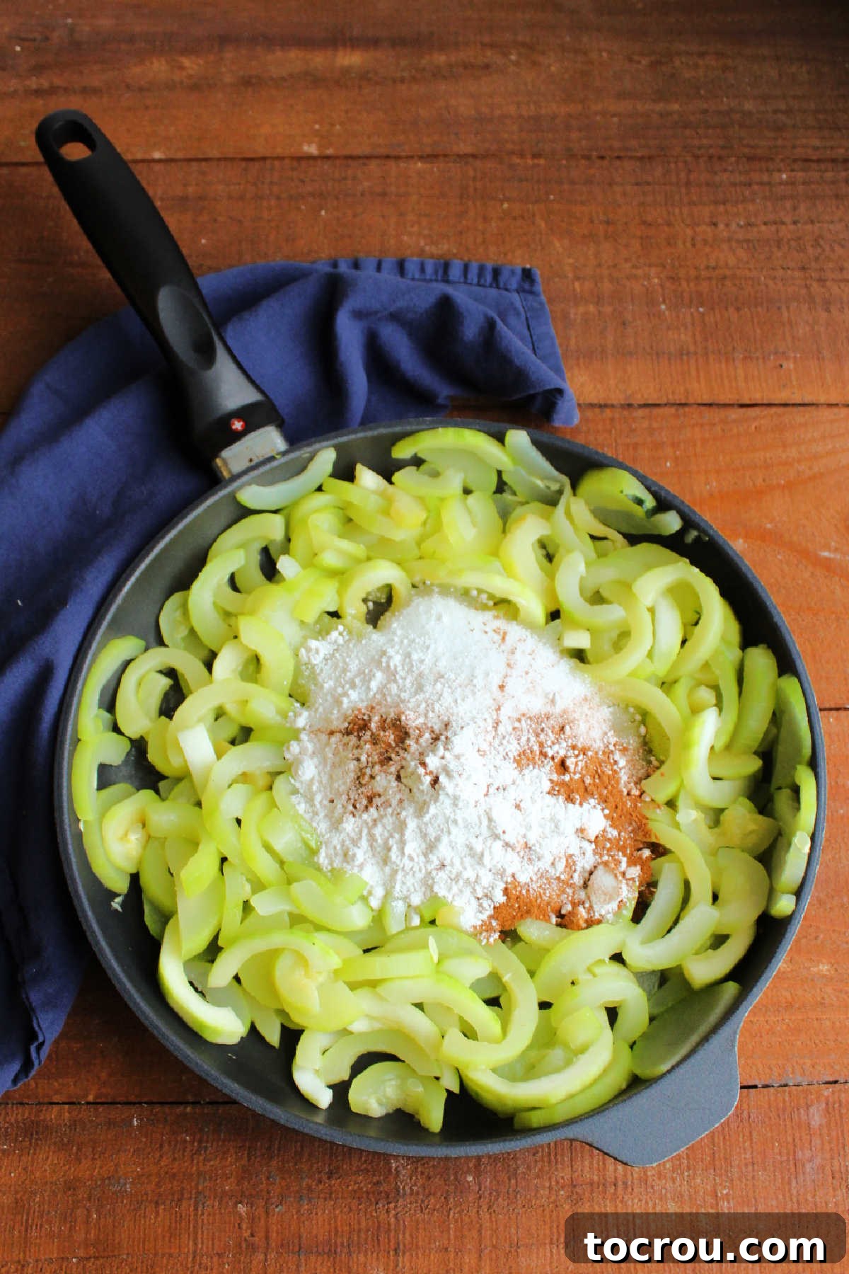 Cooked zucchini slices, infused with sugar, flour, and cinnamon, are being gently mixed in a skillet, ready for the pie crust.