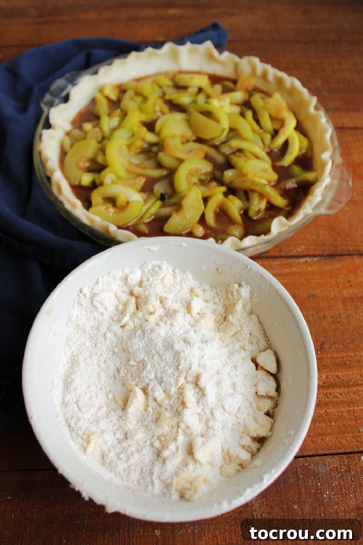 A bowl of buttery, sweet crumb topping sits invitingly beside a pie crust generously filled with the spiced zucchini mixture.