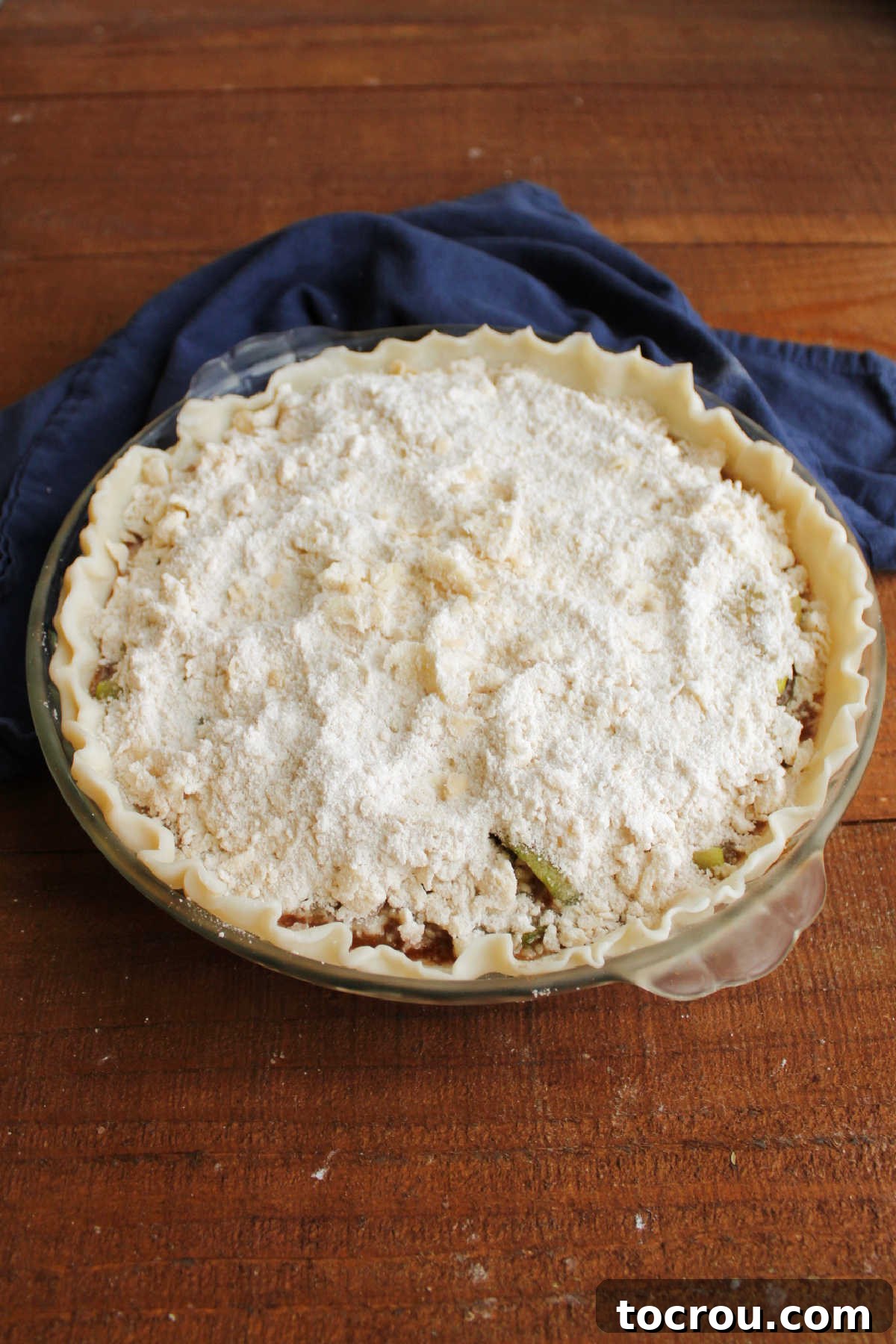 An unbaked zucchini pie, generously crowned with a golden crumb topping, sits ready to enter the oven and transform into a delectable dessert.