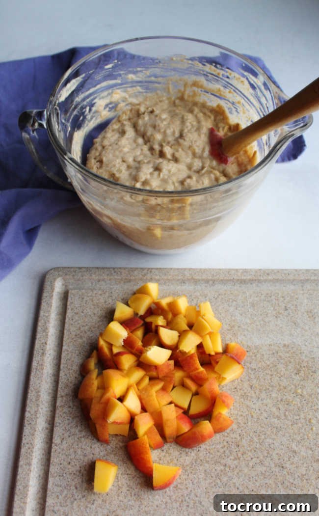 Muffin batter in a mixing bowl next to a cutting board with freshly chopped peaches.
