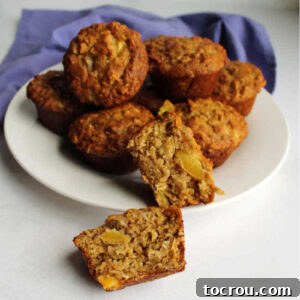 Plate of peach muffins with one cut in half in the front showing the chunks of fresh peach inside.