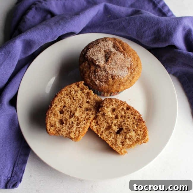 Easy Cinnamon Muffins with Brown Sugar Two cinnamon sugar muffins on a plate, one cut in half showing soft interior.