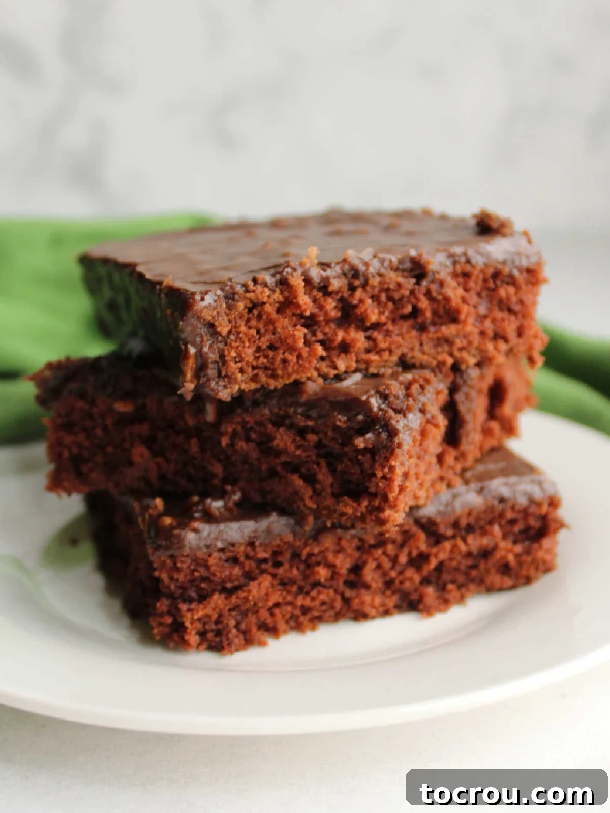 Stacked Chocolate Texas Sheet Cake Slices A stack of three pieces of chocolate Texas sheet cake with rich chocolate icing on top.