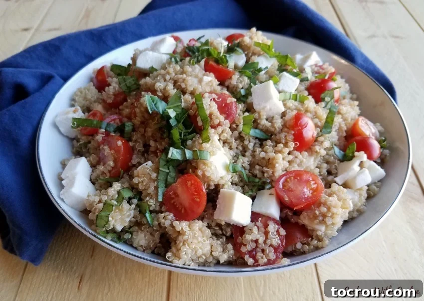 Close-up side view of a bowl of colorful Caprese Quinoa Salad, showing the texture of quinoa, diced mozzarella, and halved cherry tomatoes.