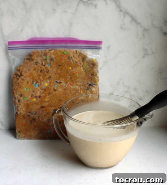 A bowl of peanut butter ice cream base sits beside a plastic bag filled with frozen monster cookie dough mixture, perfectly prepped for making ice cream.