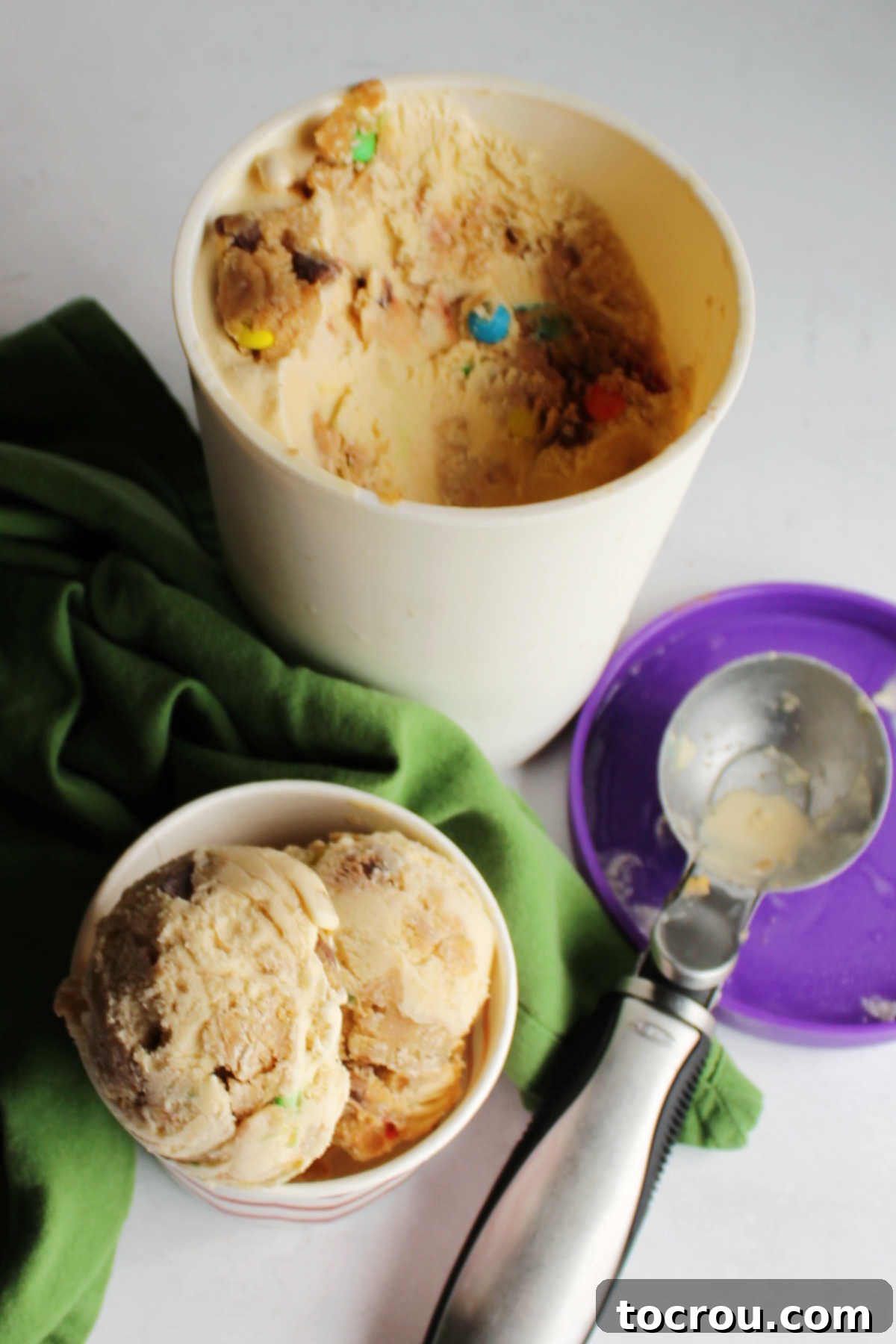 Scoops of monster cookie dough ice cream served in a bowl, with a larger container holding more homemade ice cream in the background.