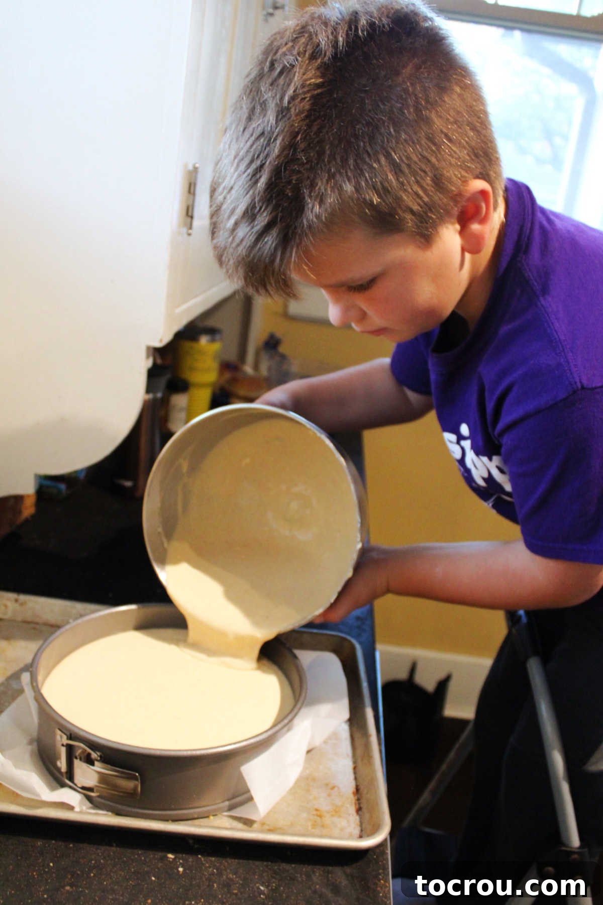 The smooth, apple butter condensed milk cheesecake mixture being carefully poured into a prepared springform pan with a crust.