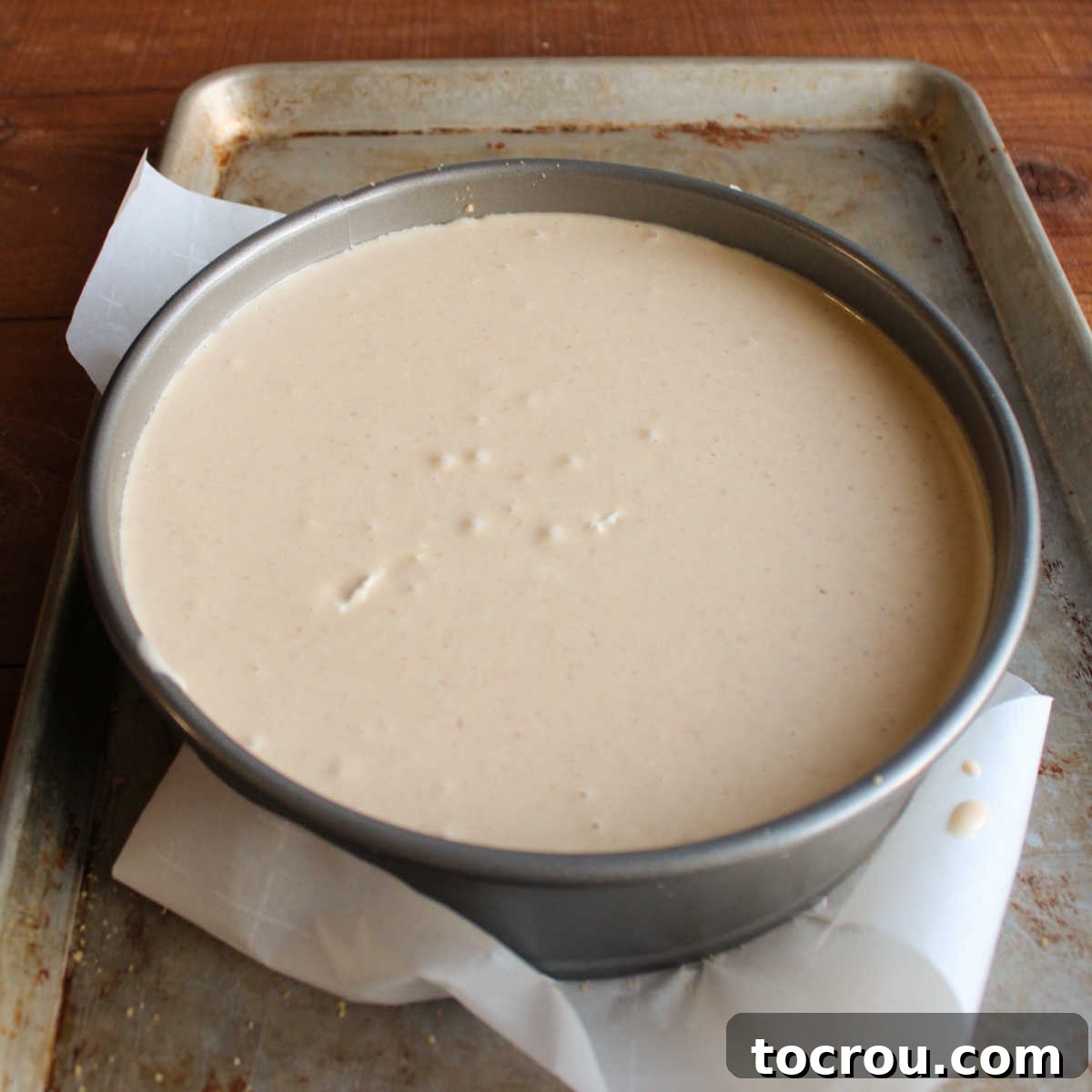 An unbaked apple butter cheesecake in a springform pan, resting on a baking sheet, ready for the oven.