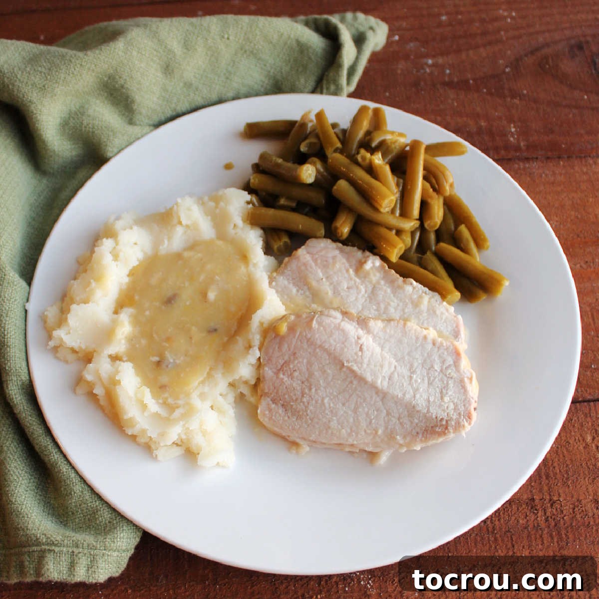 Fork Tender Pork Loin with Velvety Gravy 2 Dinner plate with slices of slow cooked pork loin, mashed potatoes and gravy and green beans.