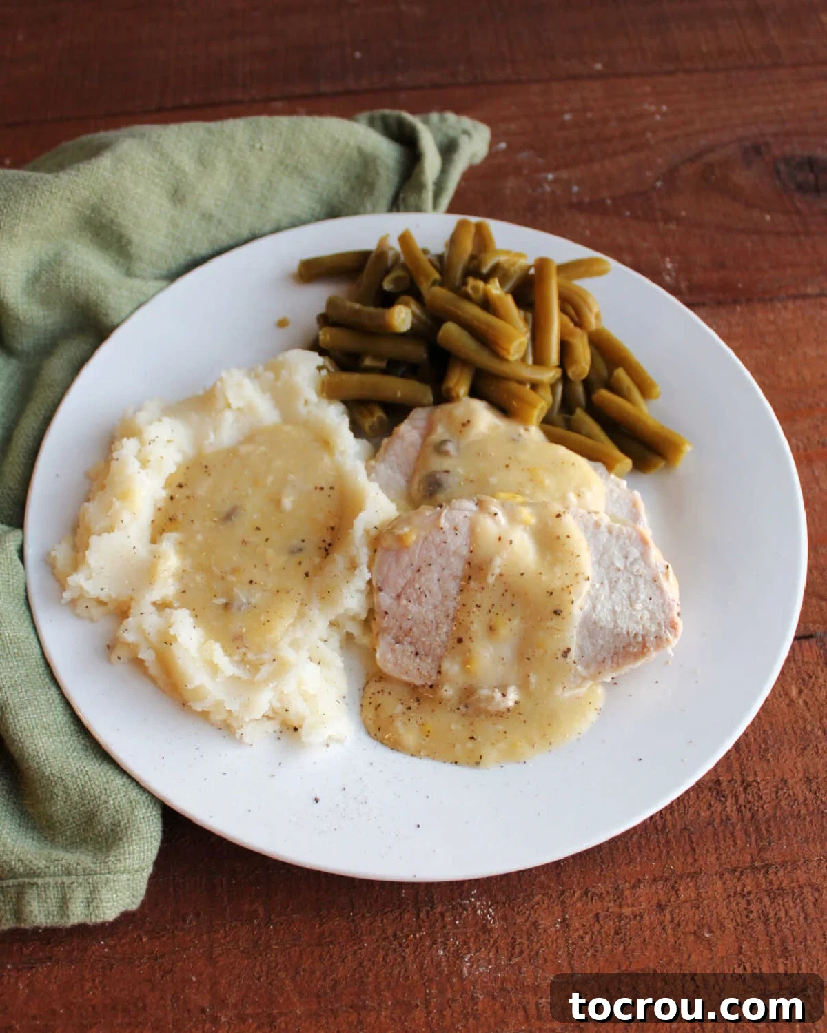 Fork Tender Pork Loin with Velvety Gravy 8 Slow cooker pork loin slices served with creamy gravy, mashed potatoes and gravy and green beans ready to eat.