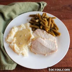 Dinner plate with slices of slow cooked pork loin, mashed potatoes and gravy and green beans.