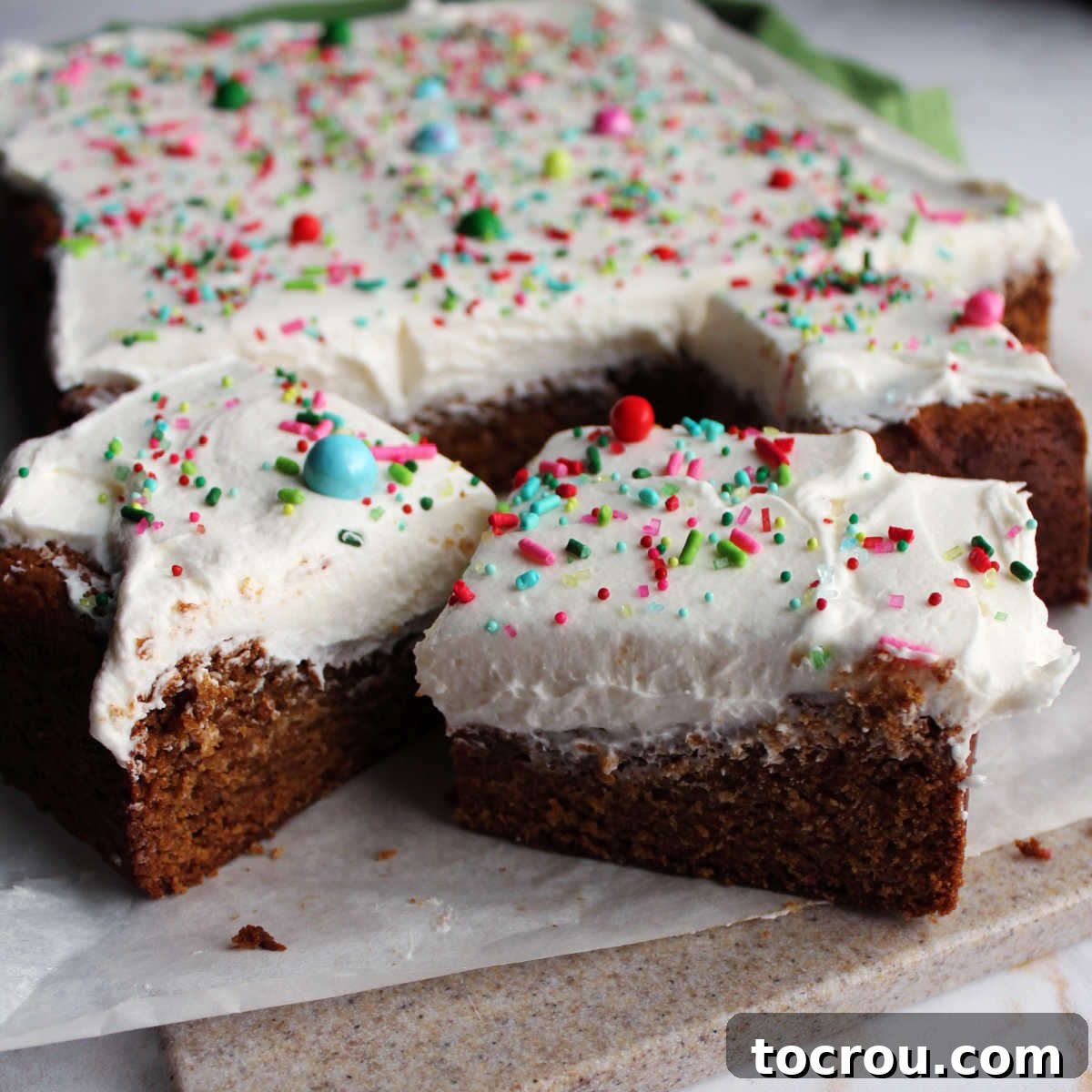 Gingerbread cookie bars with fluffy white buttercream frosting and colorful sprinkles on top, artfully arranged for a festive look.