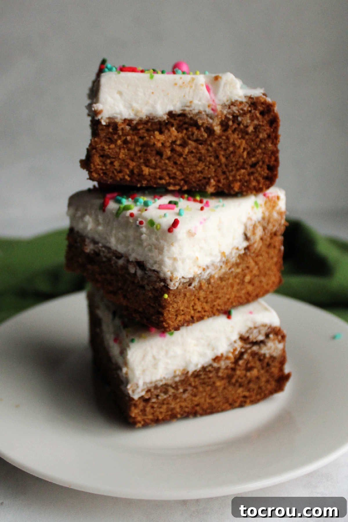 A beautiful stack of frosted gingerbread cookie bars, adorned with white buttercream and festive sprinkles, perfect for a holiday treat.
