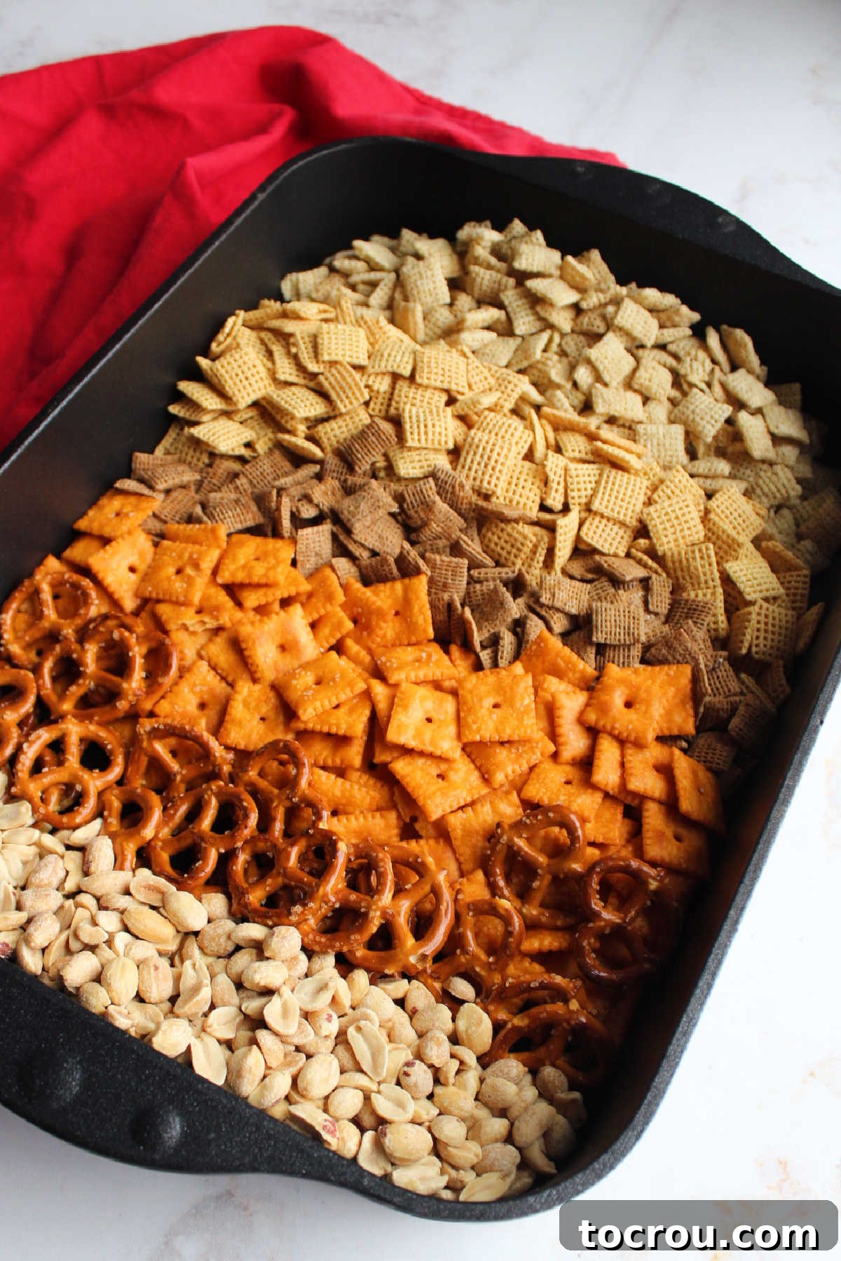 Roasting pan filled with different cereals, cheese crackers, pretzels and peanuts ready to be made into chex mix.