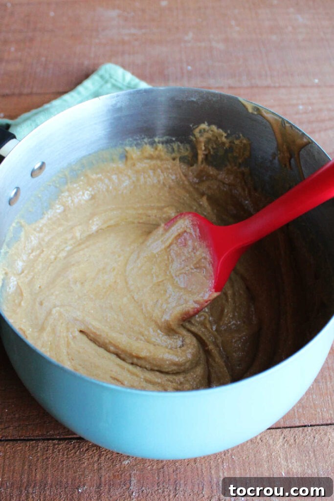 Cooked mixture of peanut butter, honey, and granulated sugar bubbling gently in a saucepan over medium-low heat, emitting a sweet aroma and ready for the next step.