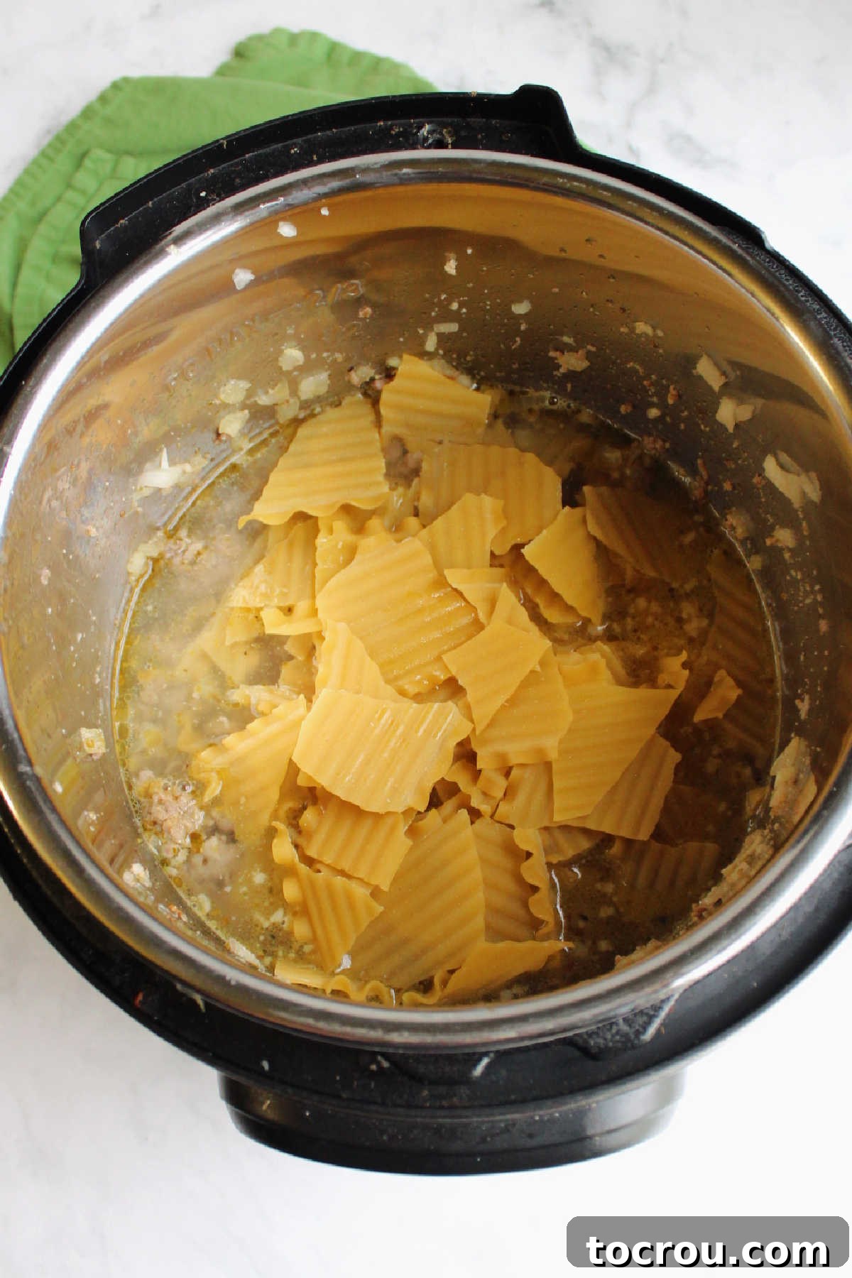 Chunks of raw lasagna noodles and chicken broth added to instant pot with sausage.