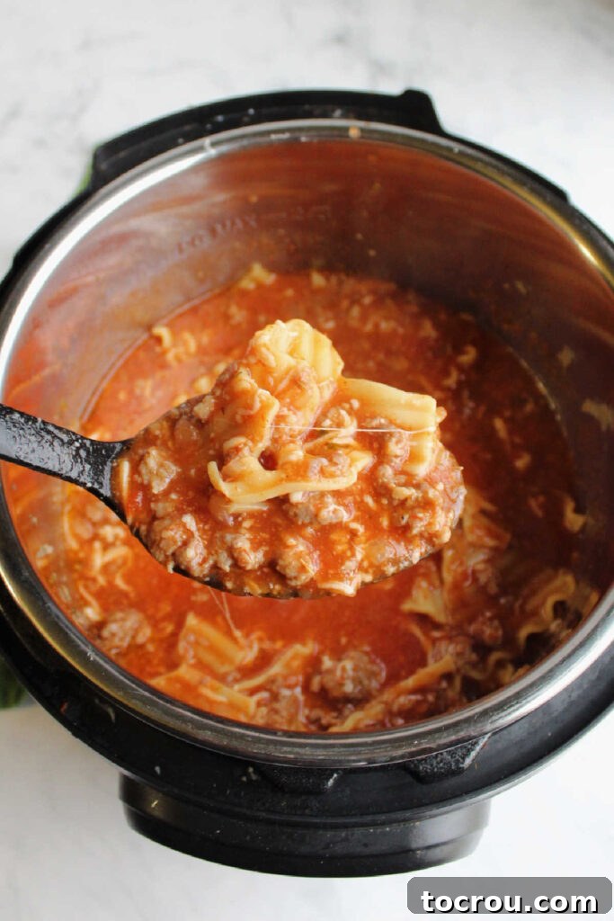 Large spoon scooping lasagna soup out of pressure cooker.