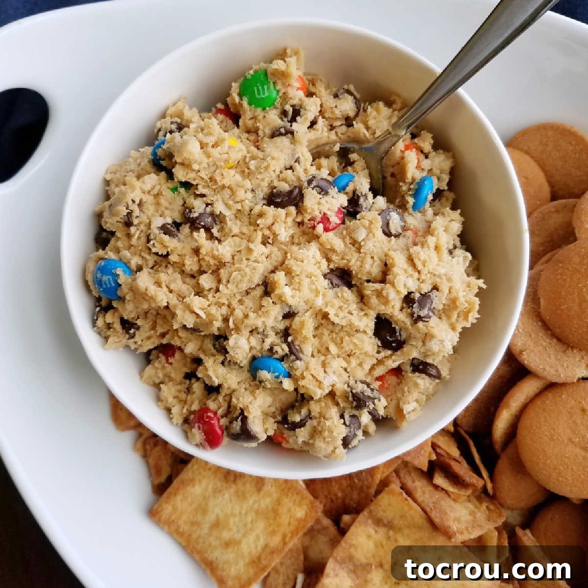 close up of bowl of monster cookie dough inspired dip with vanilla wafers and cinnamon pita chips to dip in it.