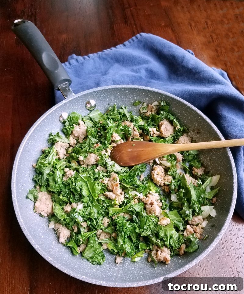 Close-up of a skillet filled with perfectly browned Italian sausage and tender, wilted kale, ready for the quiche filling.