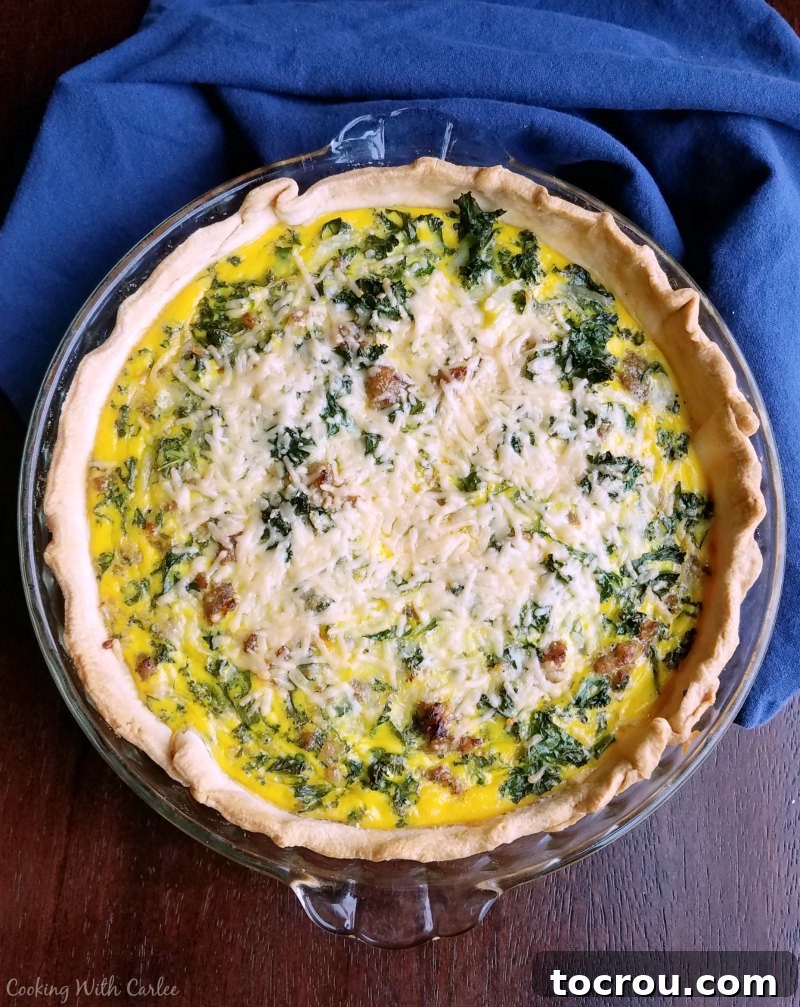 A freshly baked Sausage and Kale Quiche with a beautiful golden crust, featuring visible flecks of green kale and a bubbly, melted cheese topping.