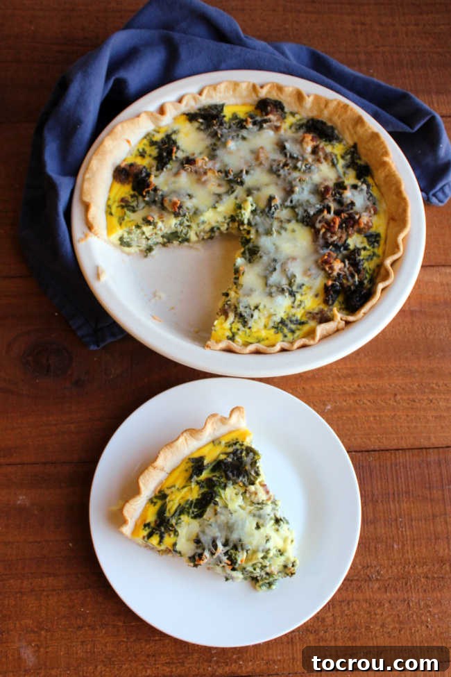 A perfect slice of Sausage and Kale Quiche on a plate, showcasing its layers, with the remaining quiche in the pan in the background.