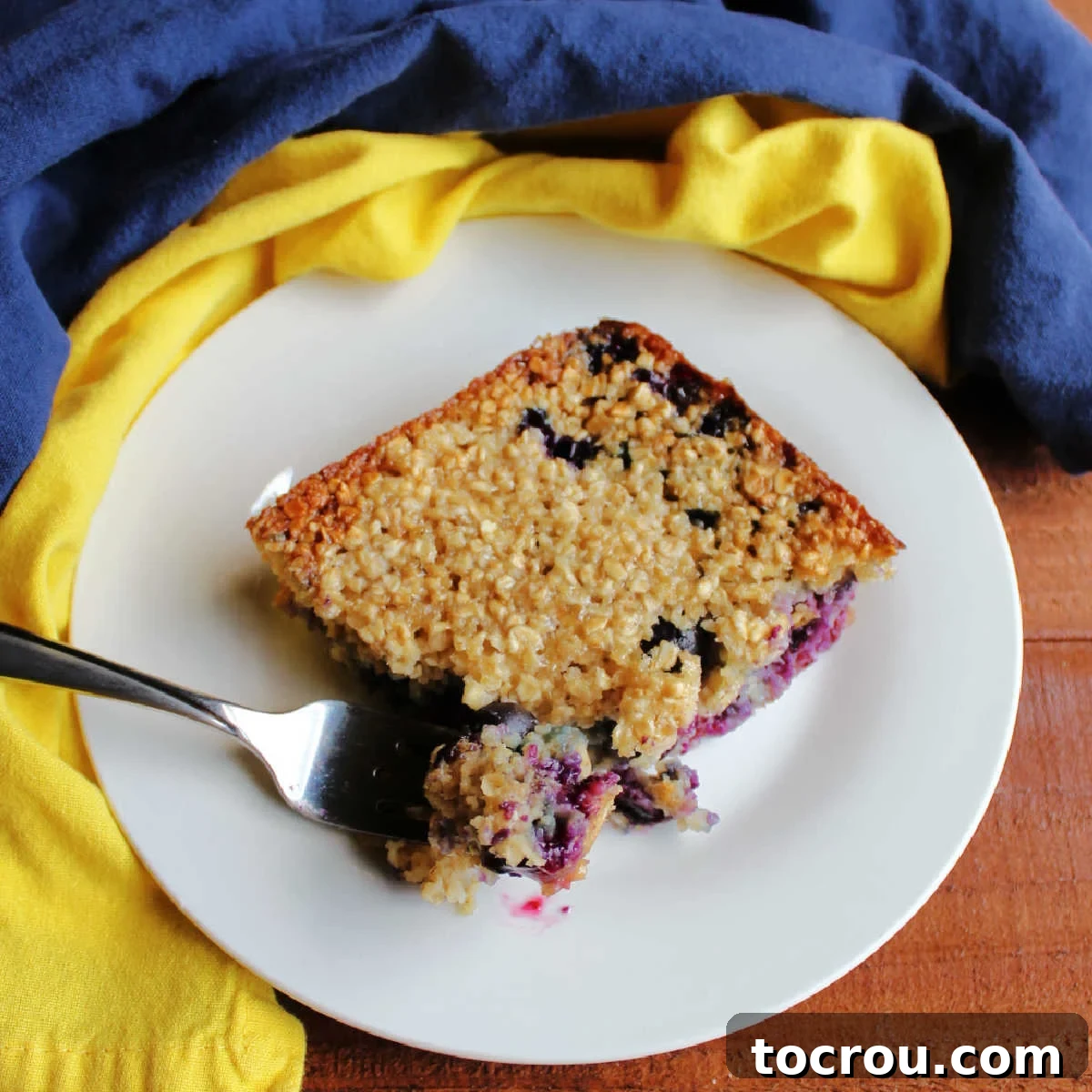 Bright Lemon Blueberry Baked Oatmeal 2 A fork lifts a bite of lemon blueberry baked oatmeal, revealing its soft texture and large, juicy blueberries, ready to be savored.