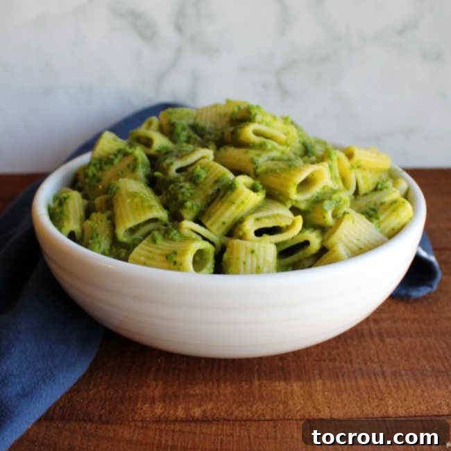 Bowl of large pasta tossed in vibrant green sauce made from a delicious mixture of garlic scapes and fresh spinach.