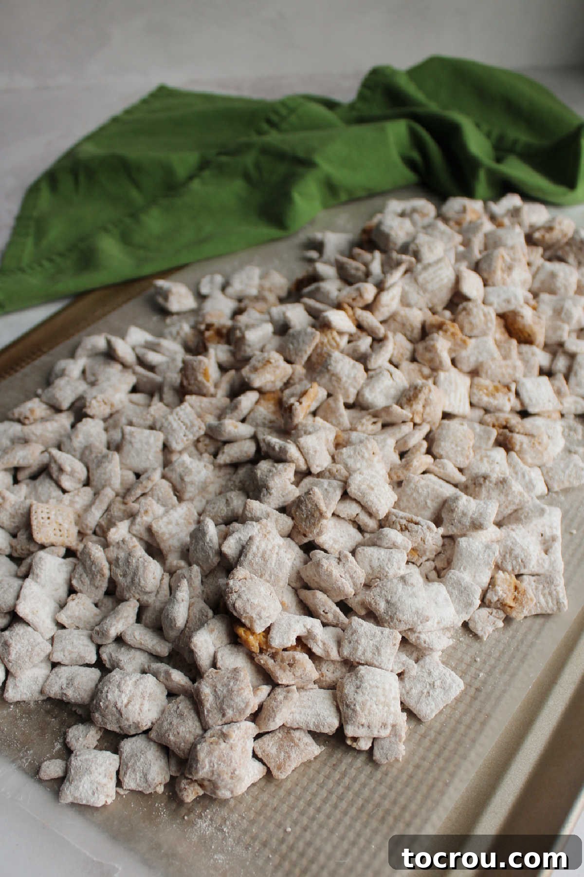 Powdered sugar coated maple cinnamon muddy buddies spread out on wax paper to set.