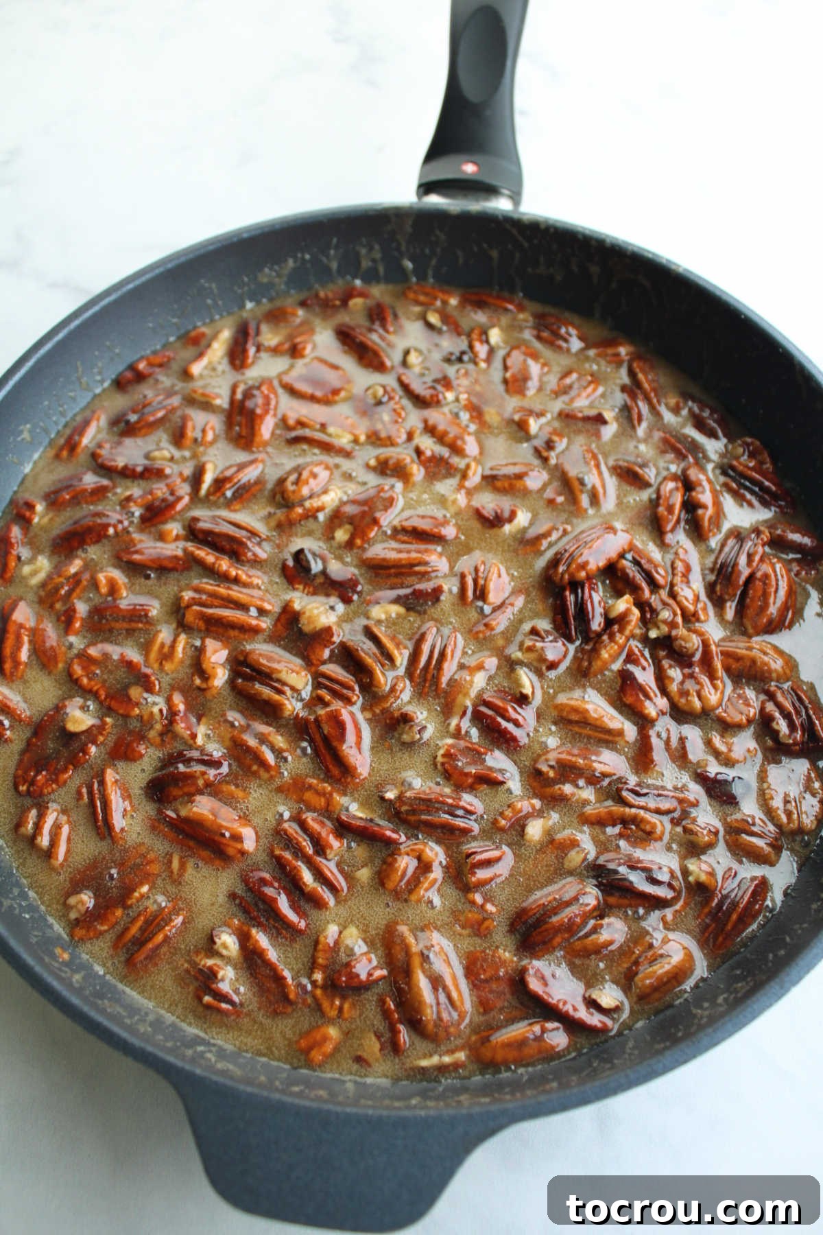 Skillet filled with brown sugar, butter, cream and pecan mixture ready to go on cheesecake.