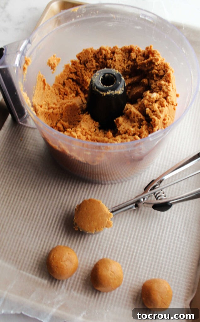 Using a small cookie scoop to portion out the peanut butter cookie ball mixture onto a baking sheet.