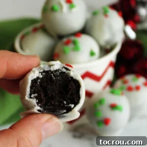 Hand holding white chocolate coated Oreo truffle showing smooth center of Oreo and condensed milk mixture.